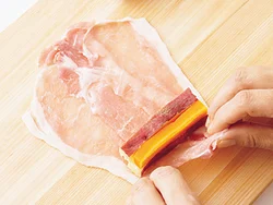 豚肉は手前と奥の幅が同じになるよう、上下を交互にして重ねて大きな１枚にする。２色の野菜は断面が市松模様になるようにのせてから、くるくる巻く。