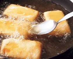 粉をまぶした豆腐に油をかけながら揚げる。ころもがふっくらして、ボリュームが出せる。
