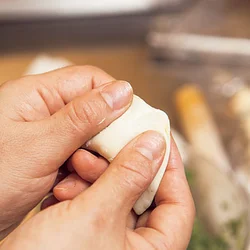 あんを皮の中央にのせて半分に折りたたんで包んでから、両手で皮の端を中央に向けて寄せて、形づくる。