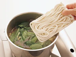 つゆができ上がったところに小松菜と冷凍うどんを入れ、うどんが熱くなるまで煮る。