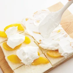 パンは並べて広げ、一度に生クリームをぬると均一にしやすい。巻き始めになるパン1切れだけは、のせる黄桃を1枚にしておく。