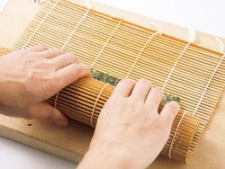 具を指で押さえながら、巻きすを持ち上げてひと巻きしたら、巻きす全体に力を入れてまんべんなく押さえるとくずれにくい。
