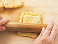 油揚げはめん棒などで押しながら２〜３回転がすと、袋状に開きやすくなる。切らずに熱湯でゆでて、余分な油を除く。