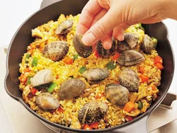 豚肉、野菜、米を加え、米が透き通るまで炒めたら平らにして、あさりをバランスよくのせる。