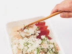 小さめのバットにラップを敷いて、刺し身、ご飯の順でのせる。ラップを敷いてあるので、あとで取り出しやすい。刺し身は１種類でもよい。