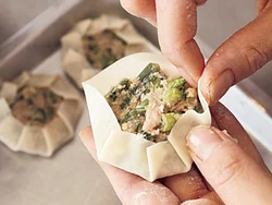 餃子の皮にあんをのせ、中央はあけながら縁を少しずつ上に折り、ひだを寄せて周囲を円く包む。