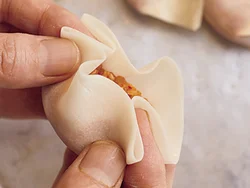 両手の人さし指で皮を内側に押し込みながら、中央に少しひだを寄せて一口で食べられるサイズに包む。