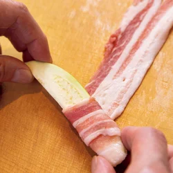なすをやや斜めに置いて転がしながら、豚肉をくるくるとすき間なく巻きつけます。